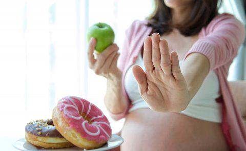 Kobieta w ciąży wybiera jabłko zamiast donatów.