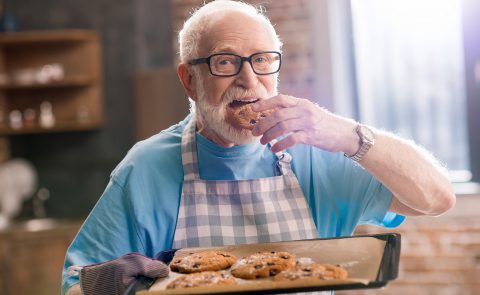 Starszy mężczyzna trzyma tacę ze świeżo upieczonymi ciastkami.
